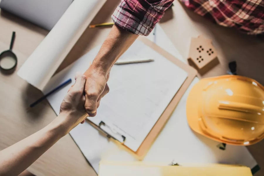 Homeowner and contractor shaking hands over project plans